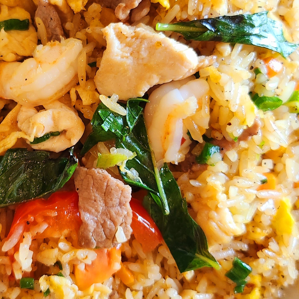 Close-up of Vietnamese fried rice with shrimp, chicken, beef, basil, and vegetables.